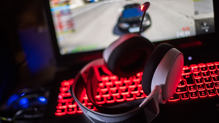 Ein Gamingheadset liegt auf einer rot leuchtenden Tastatur vor einem Bildschirm mit einem Autorennspiel