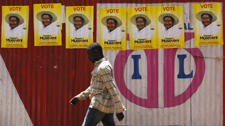 Mann läuft entlang einer Mauer mit Wahlplakaten von Museveni