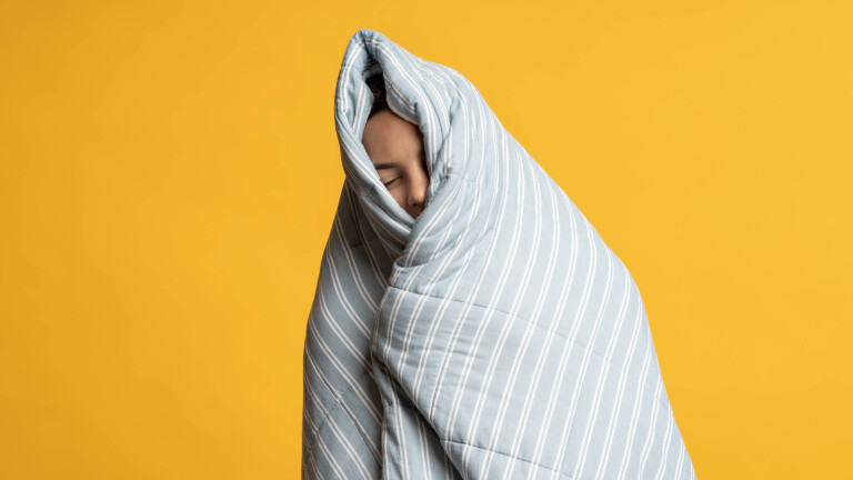 Aufwachvorgang in Bettdecke: ein eingemummelter Mensch mit geschlossenen Augen