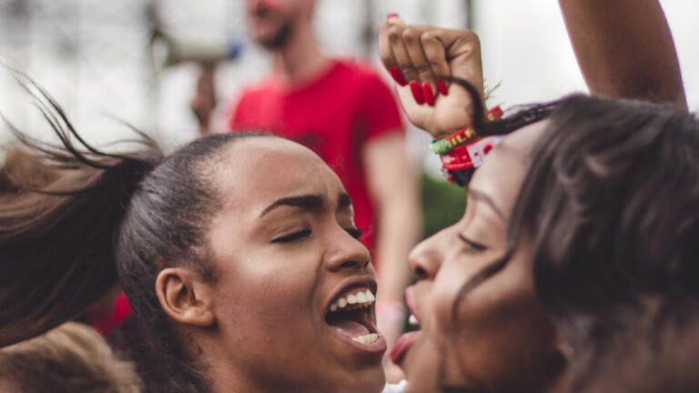Zwei Frauen reißen die Arme hoch und rufen.