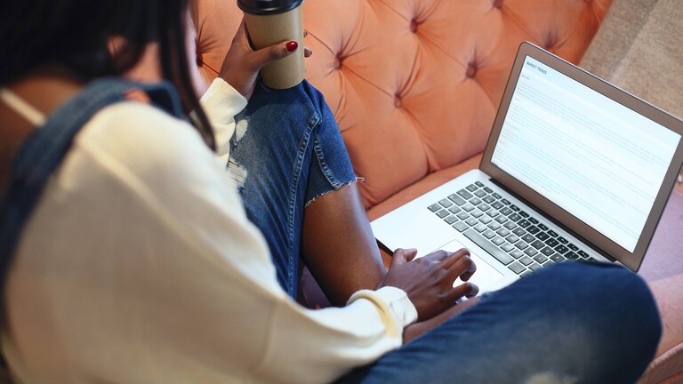 Frau sitzt mit Kaffeebecher am Laptop