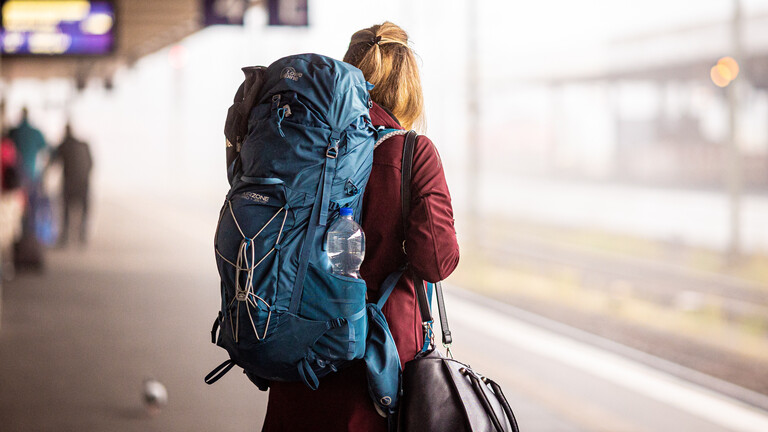 Eine Reisende steht am Morgen im Hauptbahnhof mit Rucksack.
