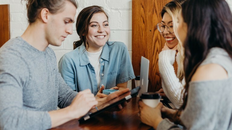 Junge Menschen stehen an einem Tisch und lachen freundlich