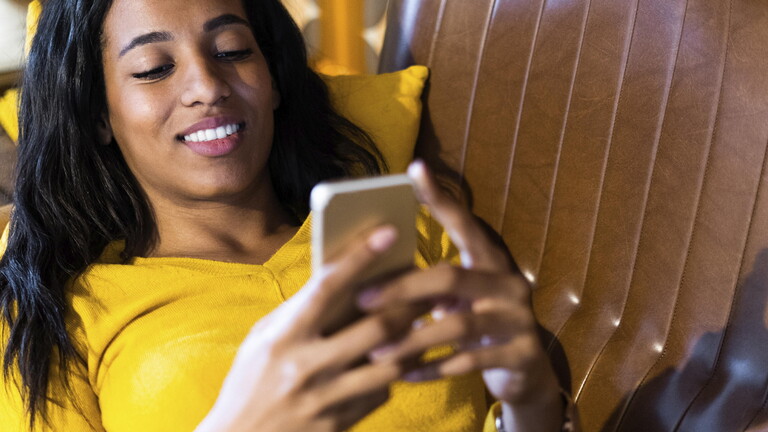 Eine junge Frau mit Smartphone chillt auf der Couch