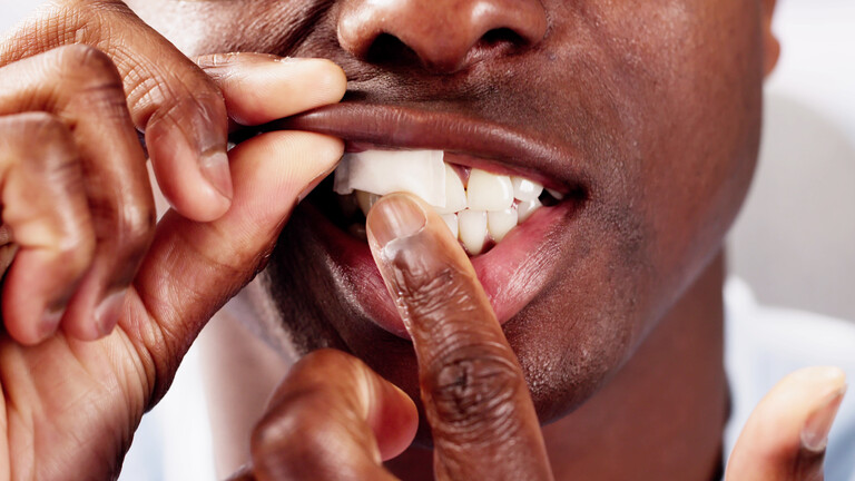 Mann schiebt sich einen weißen Tabbak-Beutel, Snus genannt, unter die Lippe.
