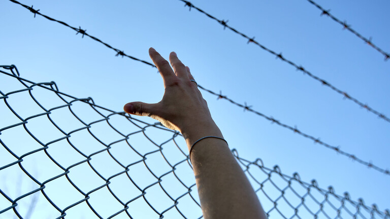 eine Hand greift an einen Stacheldrahtzaun