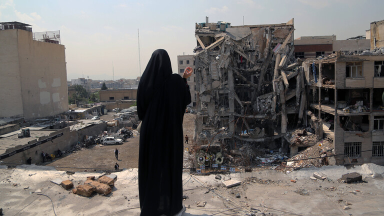 Frau blickt auf zerstörtes Haus in Iran.
