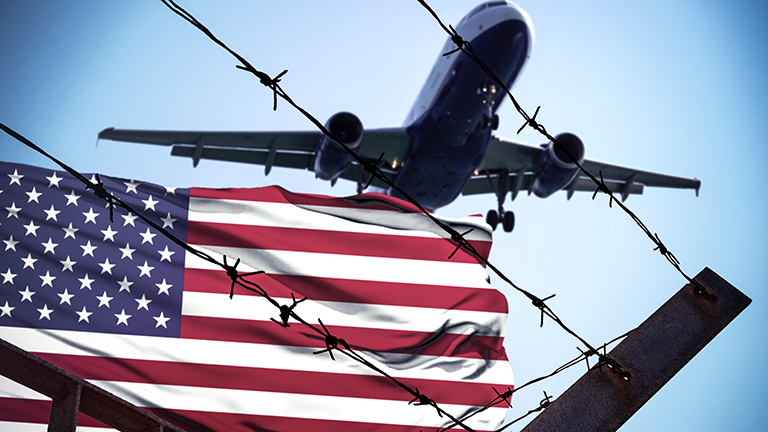 Symbolbild für Abschiebungen aus den USA. Im Vordergrund Stacheldraht und die amerikanische Flagge, darüber ein startendes Flugzeug.