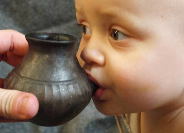 Ein Baby trinkt aus einer Rekonstruktion eines Nuckelfläschchens aus der Bronzezeit