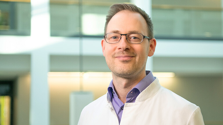 Portraitfoto von Stefan Kabisch. Er hat kurze Haare und trägt eine Brille. Ebenso einen weißen Arztkittel.