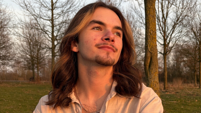 Schnappschuss von Jens, der längere Haare und ein weißes Hemd trägt, in einem Park