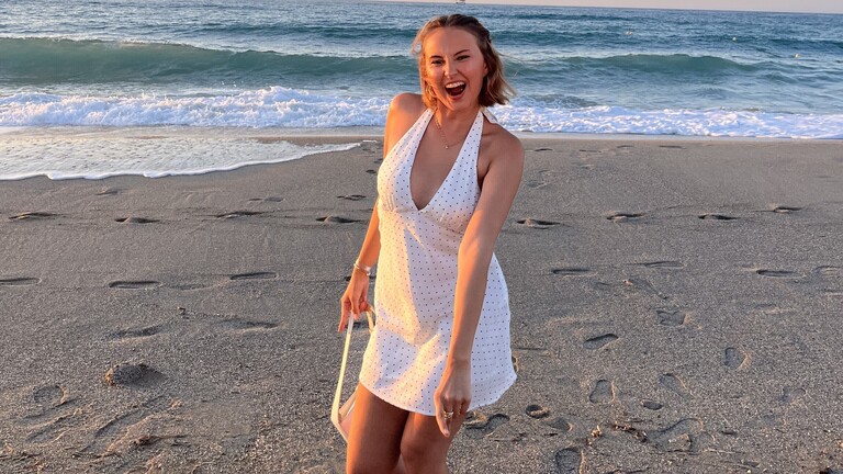 Leyo in einem Kleid bei Abendsonne am Strand. Im Hintergrund ist das Meer.