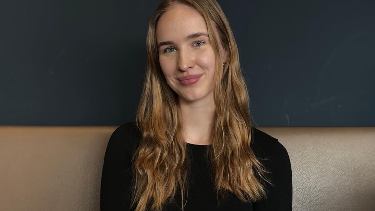 Chantal - Protagonisitin, die während des Studiums oft am Imposter-Syndrom leidet, sitzt auf einer Couch und blickt in die Kamera.