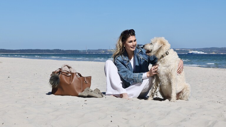 Janna sitzt mit einem Hund am Strand