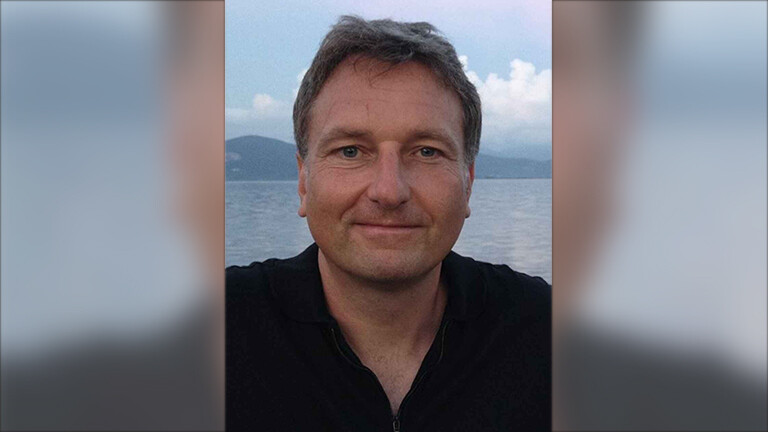 Selfie-Aufnahme von Carsten Busch. Hinter ihm sind ein See und Berge erkennbar.