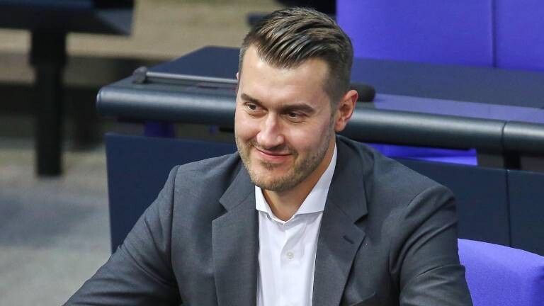 23. Bundestagssitzung - Haushaltswoche. Der Grünen-Politiker Julian Joswig sitzt im Bundestag und lächelt.
