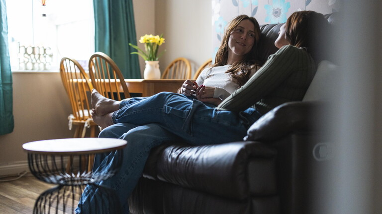 Zwei Freundinnen sitzen auf einer Couch und sprechen miteinander