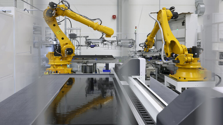 Ein orangefarbener Roboterarm hebt ein Solarmodul an