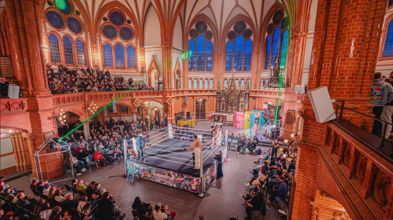 Wrestling-Veranstaltung des Vereins „enter – Junge Kulturregion Chemnitz“ // Wrestler auf Bühne mit Publikum außenherum in einer großen Halle, die wie eine ehemalige Kirche aussieht