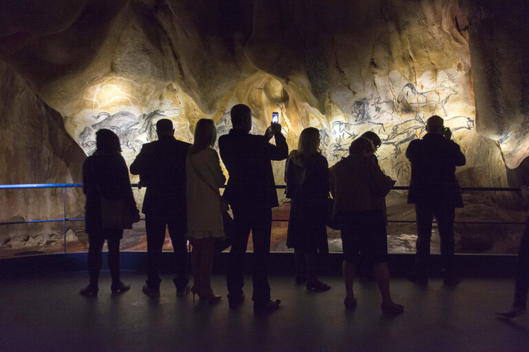 Besucher der Chauvet Grotte 2 stehen vor Malereien und machen Fotos mit ihren Smartphones. Es ist eine Nachbildung der original Chauvet-Höhle.