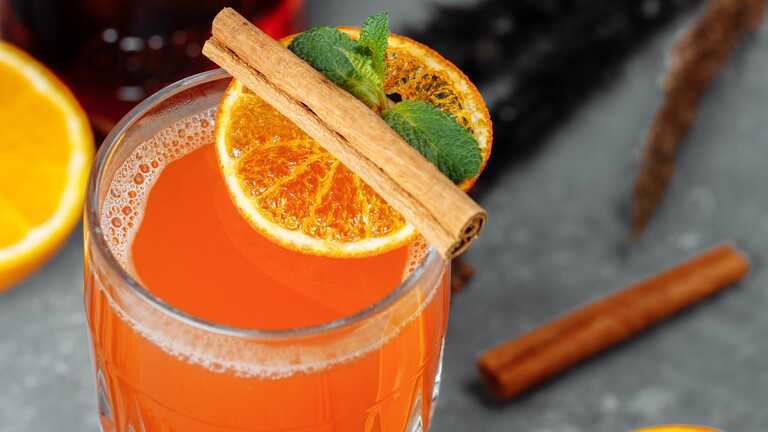 Orangefarbenes Getränk mit Orangenscheibe und Zimtstange