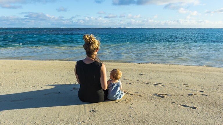 Eine Frau und ein Kind sitzen am Strand und schauen auf das Meer