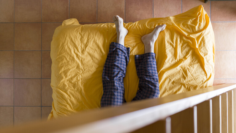 Beine eines Mannes auf einem Bett, der Oberkörper ist nicht zu sehen