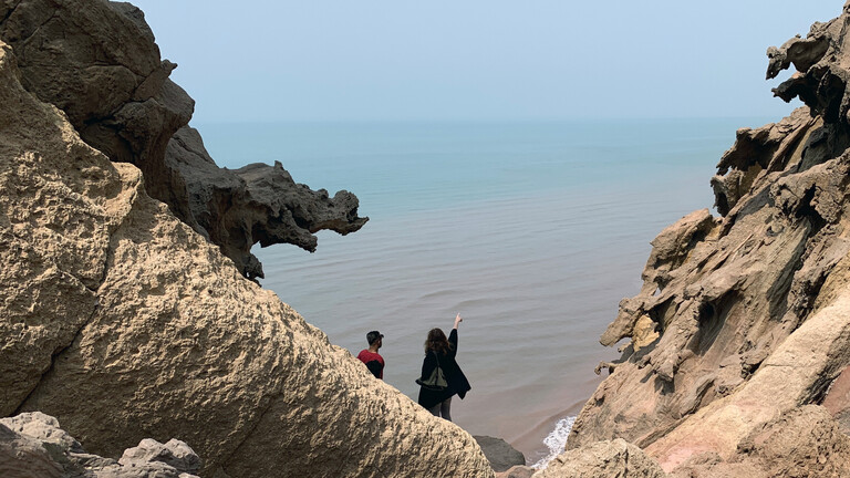 Zwei Personen blicken und deuten von der Insel Hormus in Südiran auf die Straße von Hormus am Persischen Golf.