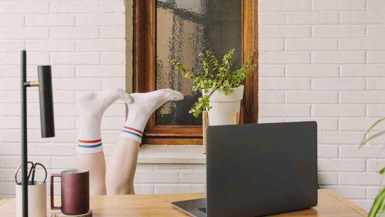 Füße mit weißen Tennisocken ragen über Schreibtisch, auf dem ein Laptop steht