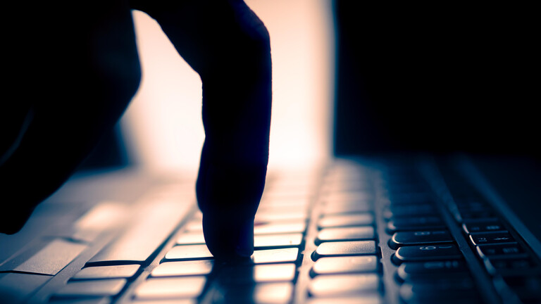 Finger tippt auf Tastatur, dunkle Umgebung und Gegenlicht