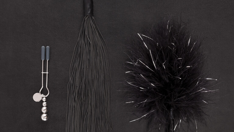 Schwarze Sextoys, darunter eine Peitsche, auf schwarzem Hintergrund