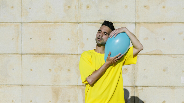 Mann in gelben Tshirt umarmt blauen Luftballon