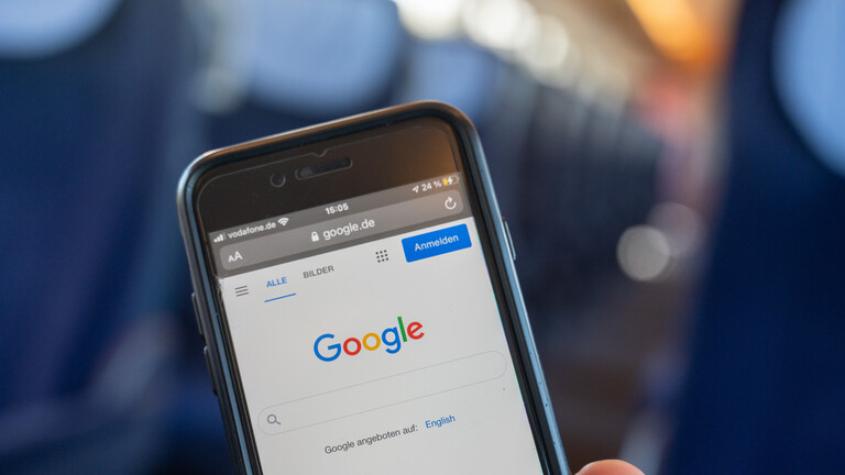 Ein Mann hält ein Handy in der Hand, auf dem Display ist die Google Homepage zu sehen
