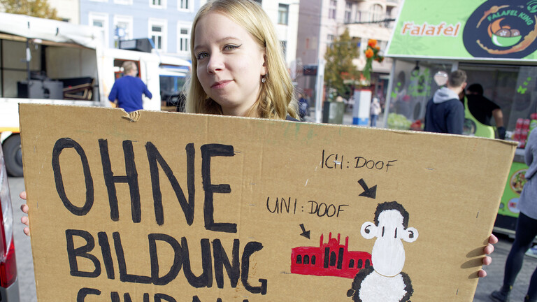 Eine Frau hält ein Plakat in die Höhe, darauf steht: Ohne Bildung sind alle doof!