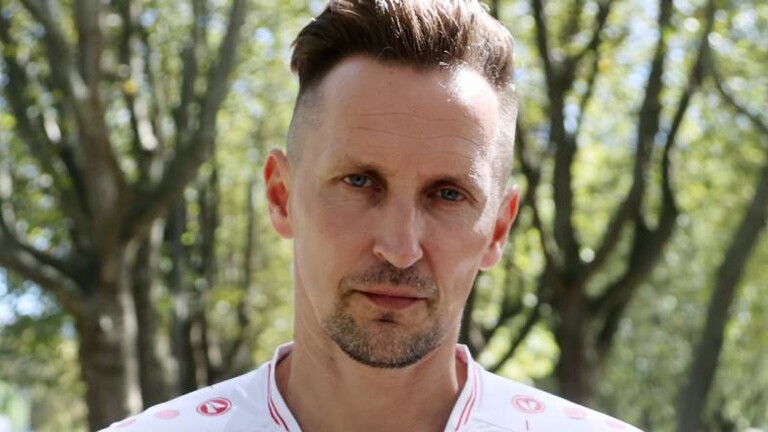 Thomas Melchior steht auf einem Weg mit Bäumen. Er trägt ein weiß-rotes Fußball-Trikot vom VfB Stuttgart. Darauf ist Werbung für ein Sportwetten-Anbieter, die überklebt ist.