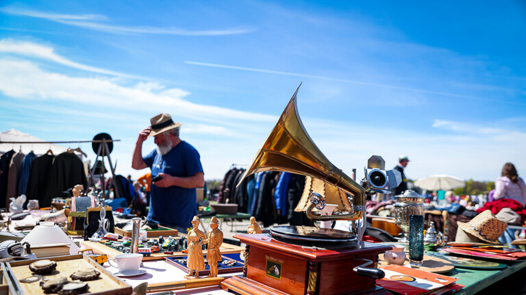Auf einem Flohmarkt in München steht auf einem Stand ein Grammofon. Darüber ein blauer Himmel.