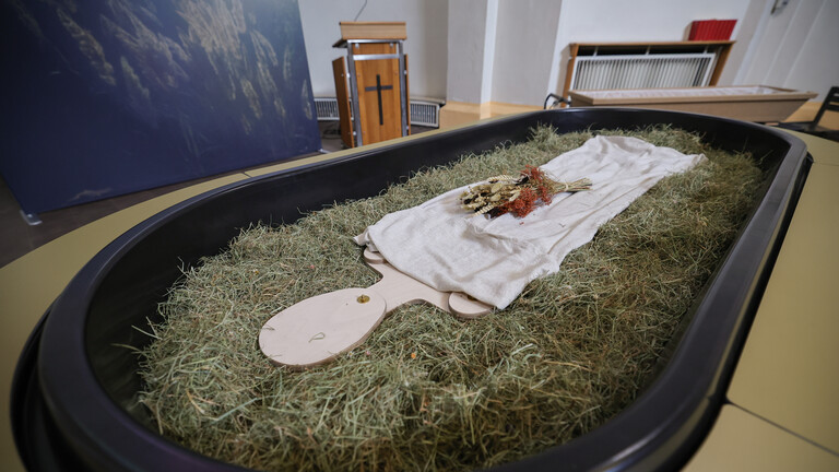 Heu, Stroh, Blumen und eine Holzfigur liegen in einem sogenannten Kokon, der neuen Bestattungsform "Reerdigung"