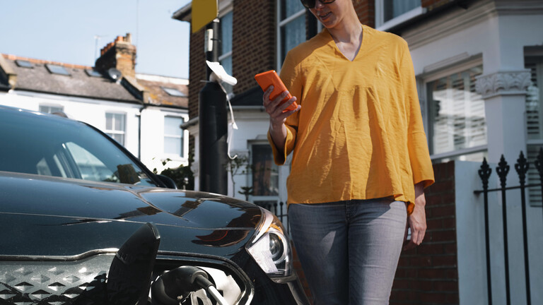 Frau mit Handy vor Auto