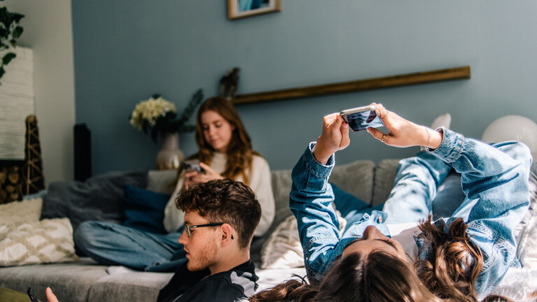 Drei junge Leute liegen auf Sofas und tippen in ihre Handys