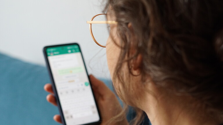 Eine junge Frau hält ihr Smartphone in der Hand und liest eine Whatsapp-Nachricht