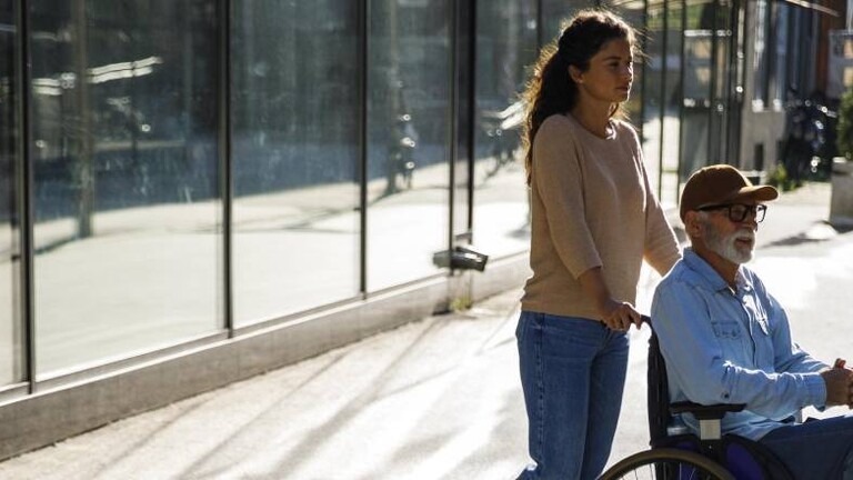 Junge Frau schiebt älteren Mann im Rollstuhl