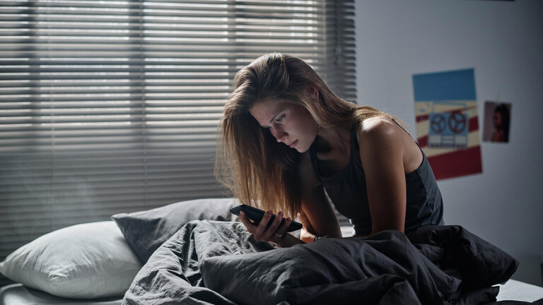 Eine junge Frau schaut erschrocken auf ihr Smartphone