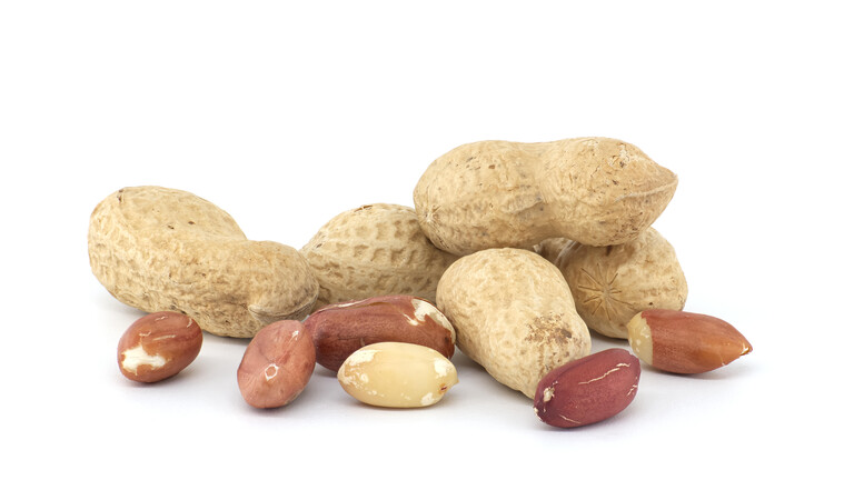 Pile of shelled and unshelled dried peanuts scattered on white background