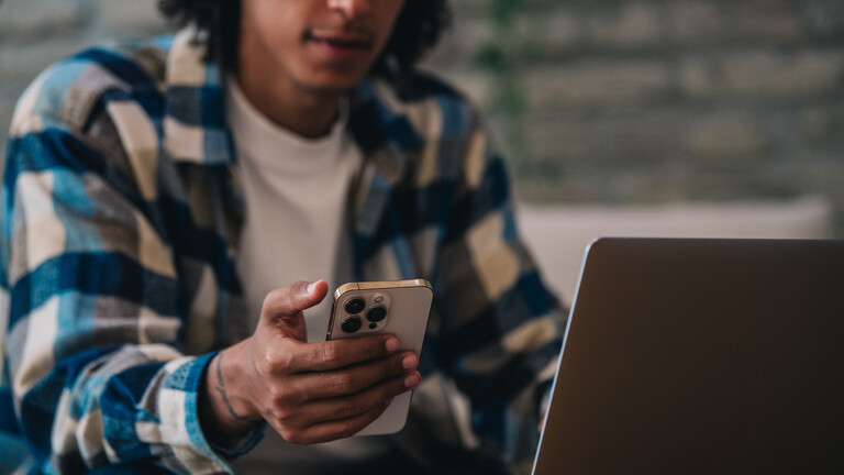 Mann sitzt mit Smarthphone vor Laptop