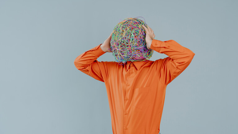 Mann im orangenem Hemd mit einem Kopf voller bunter chaotischer Gedanken statt eines Gesichts vor blauem Hintergrund.