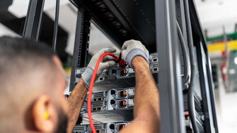 Ein Mann steht an einem Serverschrank. Er trägt Handschuhe.