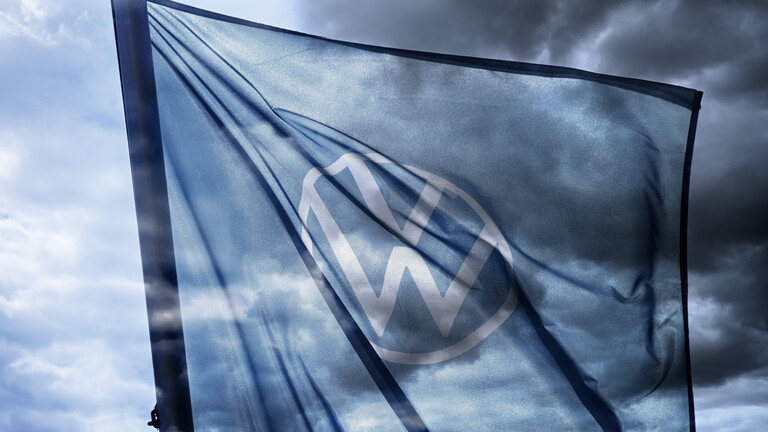 VW-Zeichen auf der Fahne eines Autohändlers, die vor dunklem Himmel weht.