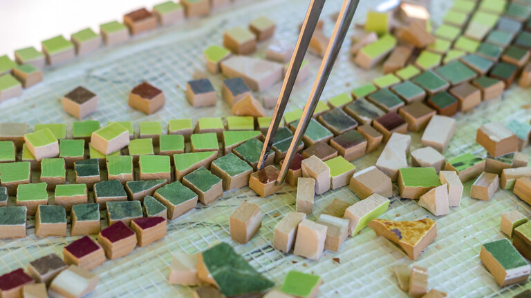 Ein Mann organisiert mit einer Pinzette ein Puzzle aus keramischen Elementen für den Bau von Keramikarbeiten.