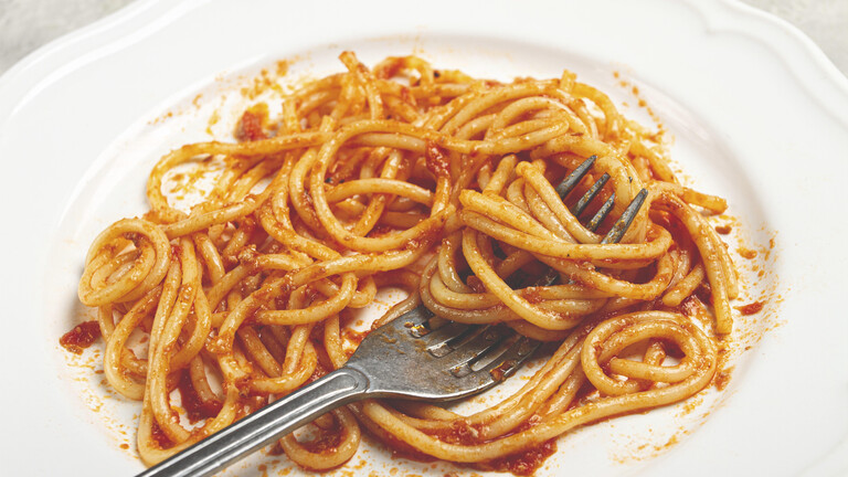 Teller mit Spaghetti und Tomatensauce, in denen eine Gabel steckt
