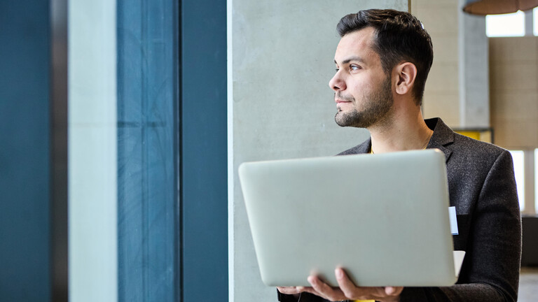 Mann mit Laptop im Arm blickt aus dem Fenster
